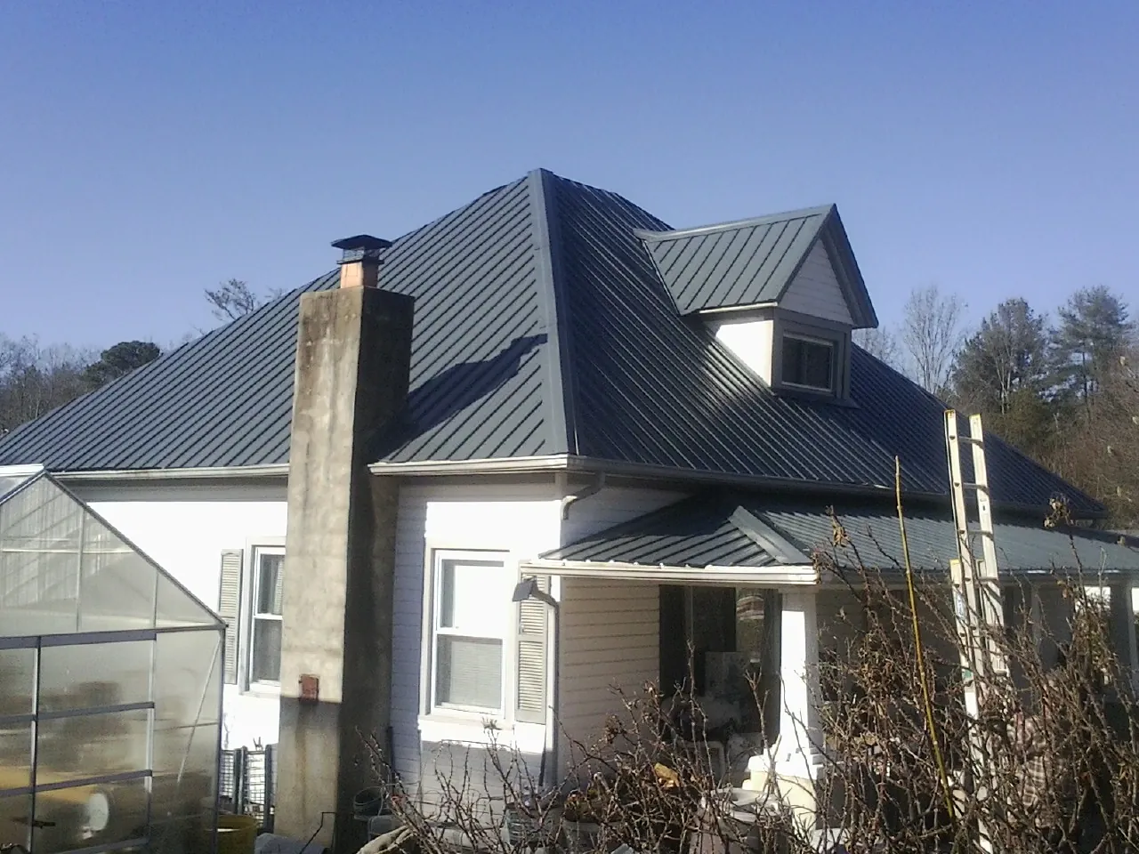 Dark blue standing seam metal roof on a white farmhouse with dormer — Slate & Tile Roof Repair by Roofing Brothers in New Kent