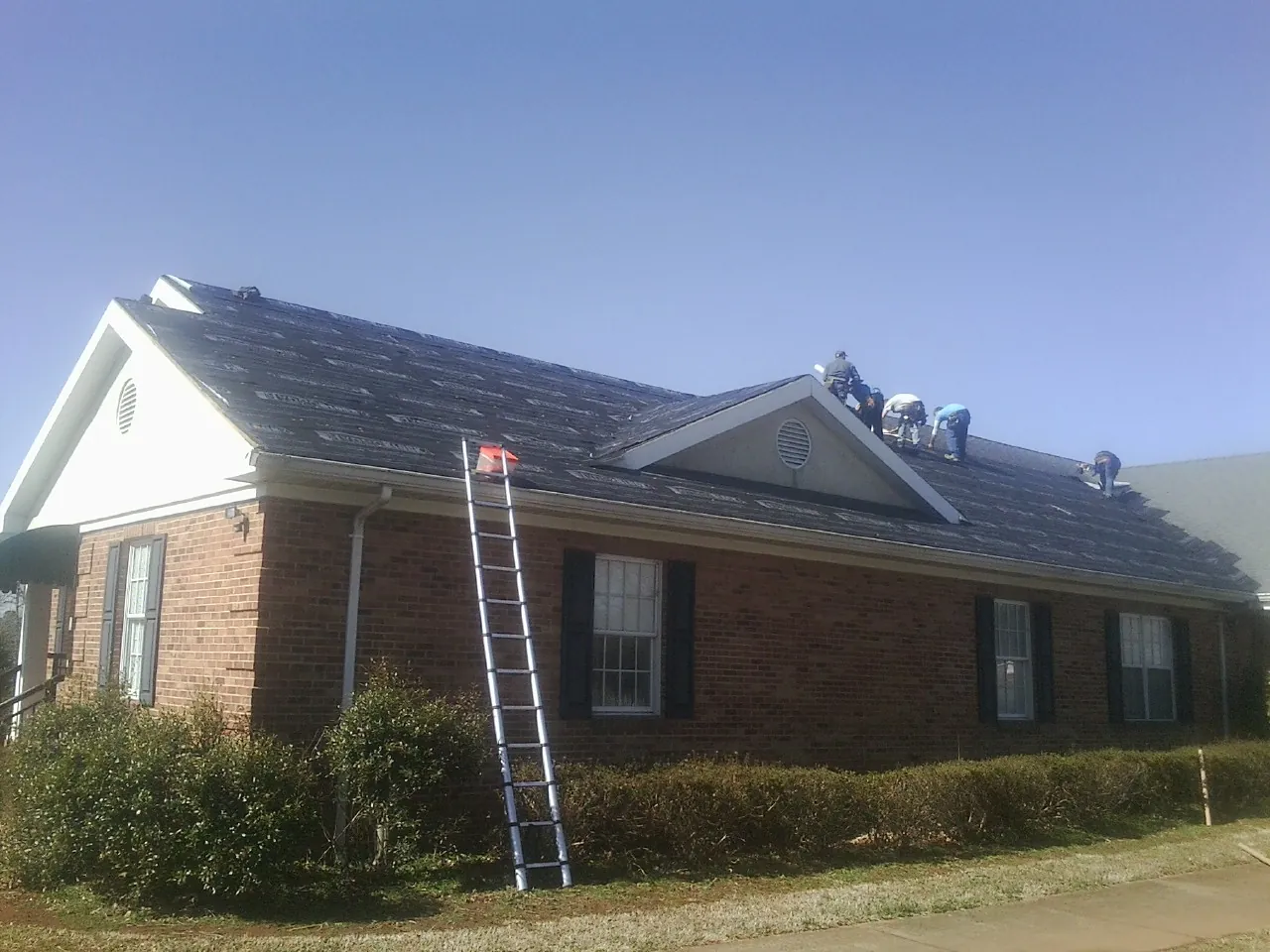 Crew tearing shingles off a brick ranch roof with a ladder set — Metal Roof Repair work by our crew in New Kent