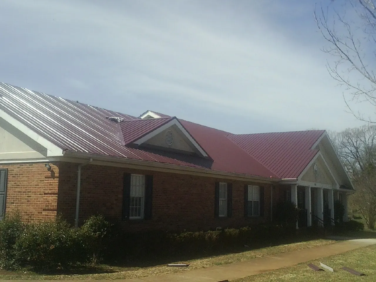 Red metal roof with gabled entries on a long brick building, from a Hail Damage Roof Repair job in New Kent