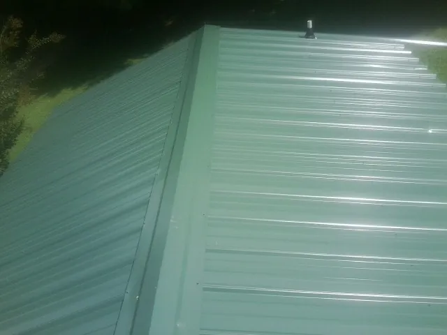 New green metal panels meeting at the ridge of a roof — Flat Roof Repair work by our crew in New Kent