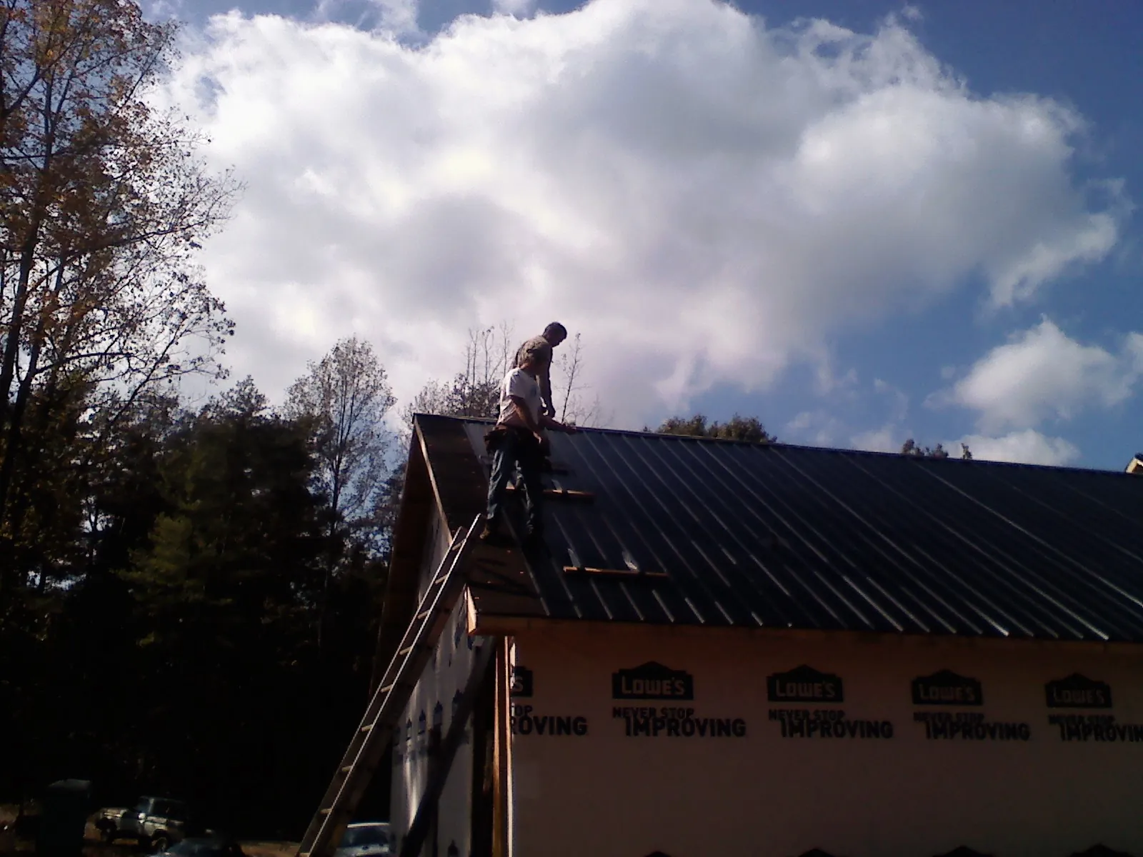 Roofer fastening dark metal panels high against a cloudy sky, from a Roof Inspection job in New Kent