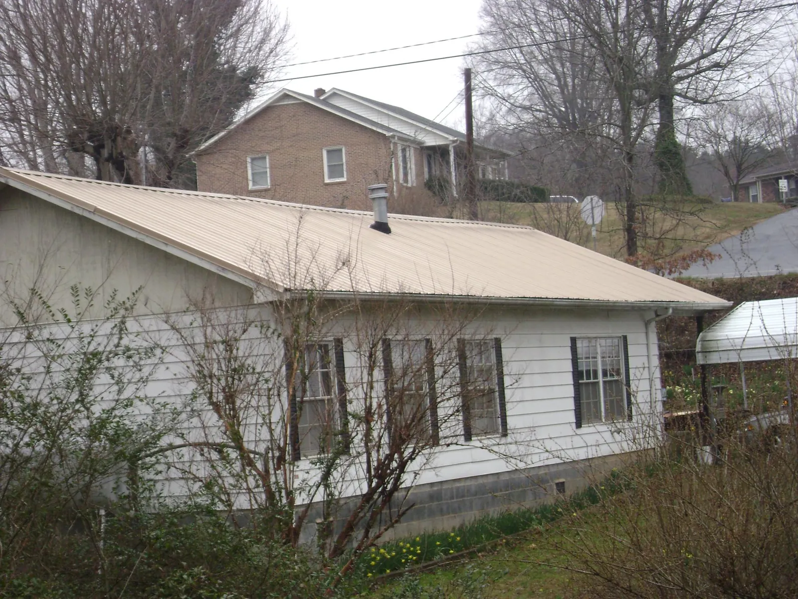 Tan metal roof on a white sided house set into a hillside — Commercial Roofing by Roofing Brothers in New Kent